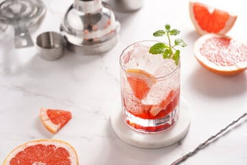 Preparation of a grapefruit alcohol free cocktail - A tumbler glass with ice cubes on marble surface with fresh mint surrounded by steel cocktail shaker and bar equipment
