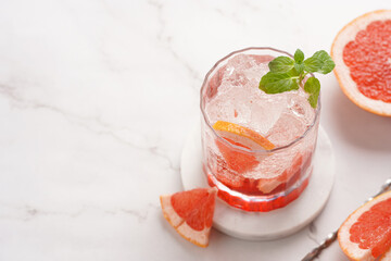 Preparation of a grapefruit alcohol free cocktail - A tumbler glass with ice cubes on marble surface with fresh mint , space for text