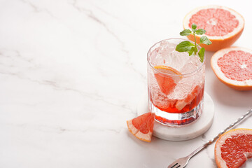 Preparation of a grapefruit alcohol free cocktail - A tumbler glass with ice cubes on marble surface with fresh mint , space for text