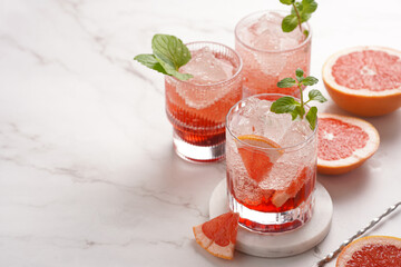 Preparation of a grapefruit alcohol free cocktail - several tumbler glasses with ice cubes on marble surface with fresh mint , space for text