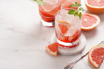 Preparation of a grapefruit alcohol free cocktail - several tumbler glasses with ice cubes on marble surface with fresh mint , space for text