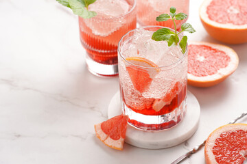 Preparation of a grapefruit alcohol free cocktail - several tumbler glasses with ice cubes on marble surface with fresh mint