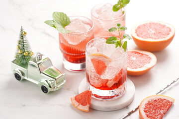 Preparation of a grapefruit alcohol free cocktail - several tumbler glasses with ice cubes on marble surface with fresh mint , christmas decoration