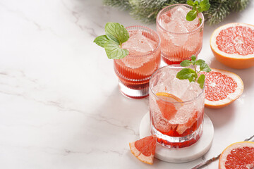 Preparation of a grapefruit alcohol free cocktail - several tumbler glasses with ice cubes on marble surface with fresh mint , christmas decoration