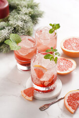 Preparation of a grapefruit alcohol free cocktail - several tumbler glasses with ice cubes on marble surface with fresh mint , christmas decoration