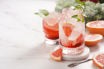 Preparation of a grapefruit alcohol free cocktail - several tumbler glasses with ice cubes on marble surface with fresh mint