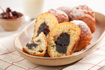Several deep fried sweet balls made of yeast dough - donuts with poppy and cherry filling on an oval off-white plate on a checkered kitchen towel. unhealthy dessert