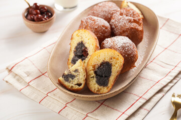 Several deep fried sweet balls made of yeast dough - donuts with poppy and cherry filling on an oval off-white plate on a checkered kitchen towel. unhealthy dessert