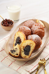Several deep fried sweet balls made of yeast dough - donuts with poppy and cherry filling on an oval off-white plate on a checkered kitchen towel. unhealthy dessert