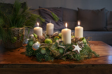 Third Advent, wreath with three burning white candles and Christmas decoration on a wooden table in front of the couch, festive home decor, copy space, selected focus