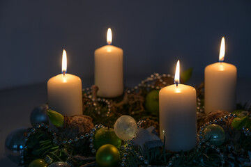 Four white Advent candles on a wreath with Christmas decoration against a dark blue background copy space, selected focus, narrow depth of field