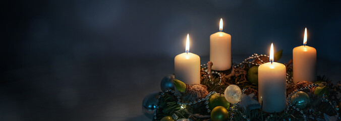 Lights in the night, four white Advent candles on a wreath with Christmas decoration against a dark...