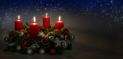 Advent wreath with red burning candles and Christmas decoration against a dark blue background with...