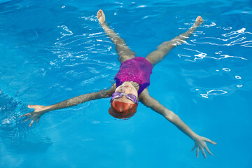 Little girl swimming and laying on water resting in indoor pool