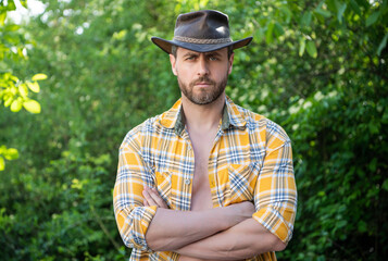 man crossed hands in cowboy hat. sexy man in checkered shirt. western man wearing hat