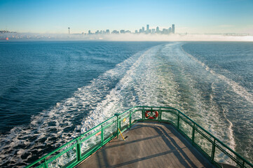 Riding the Seattle to Bainbridge Island Ferryboat at Sunrise. A popular tourist activity and a regular commuting route crossing Elliott Bay on a winter morning with the bow wake pointing to the city. - obrazy, fototapety, plakaty
