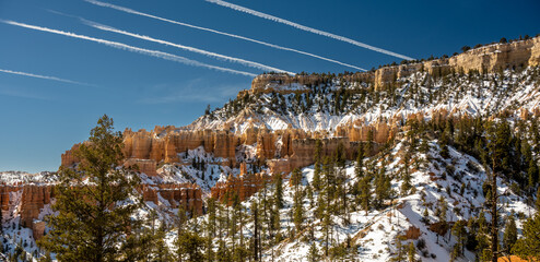 Jet Contrails Streak Across The Sky Over A Snow Covered Bryce Canyon