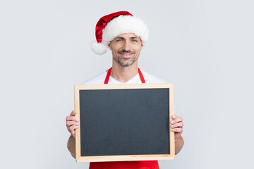 happy mature man in santa hat and apron hold blackboard with copy space
