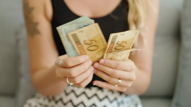 Young woman counting brazil real banknotes at home