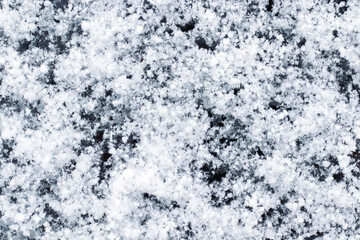 Snow grains and snowflakes are sprinkled on the black hood of the car. Fresh slightly wet snow, warm winter