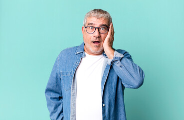 middle age senior man feeling shocked and astonished holding face to hand in disbelief with mouth...