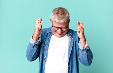 middle age senior man feeling nervous and hopeful, crossing fingers, praying and hoping for good luck