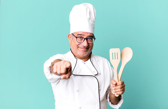 middle age senior man pointing at camera choosing you. restaurant chef with a tool concept