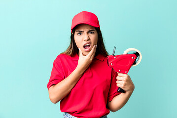 hispanic pretty woman with mouth and eyes wide open and hand on chin. packer and delivery employee