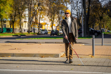 Blind man with a cane walks along a pedestrian crossing in autumn