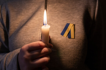 Blackout. Girl with a yellow-blue ribbon (the national symbol of Ukraine) holds a burning candle in...