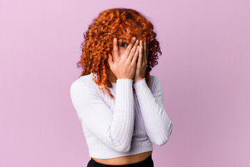 redhair pretty woman feeling scared or embarrassed, peeking or spying with eyes half-covered with...