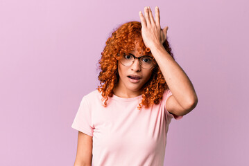 redhair pretty woman raising palm to forehead thinking oops, after making a stupid mistake or...
