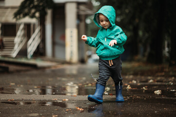 Fototapeta premium Happy boy playing outside on a rainy day wearing rubber boots and jacket