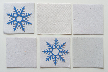 two blue paper snowflakes on stone white textured paper tiles