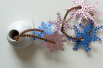 white bud vase and collection of paper snowflakes strung on pipe cleaners