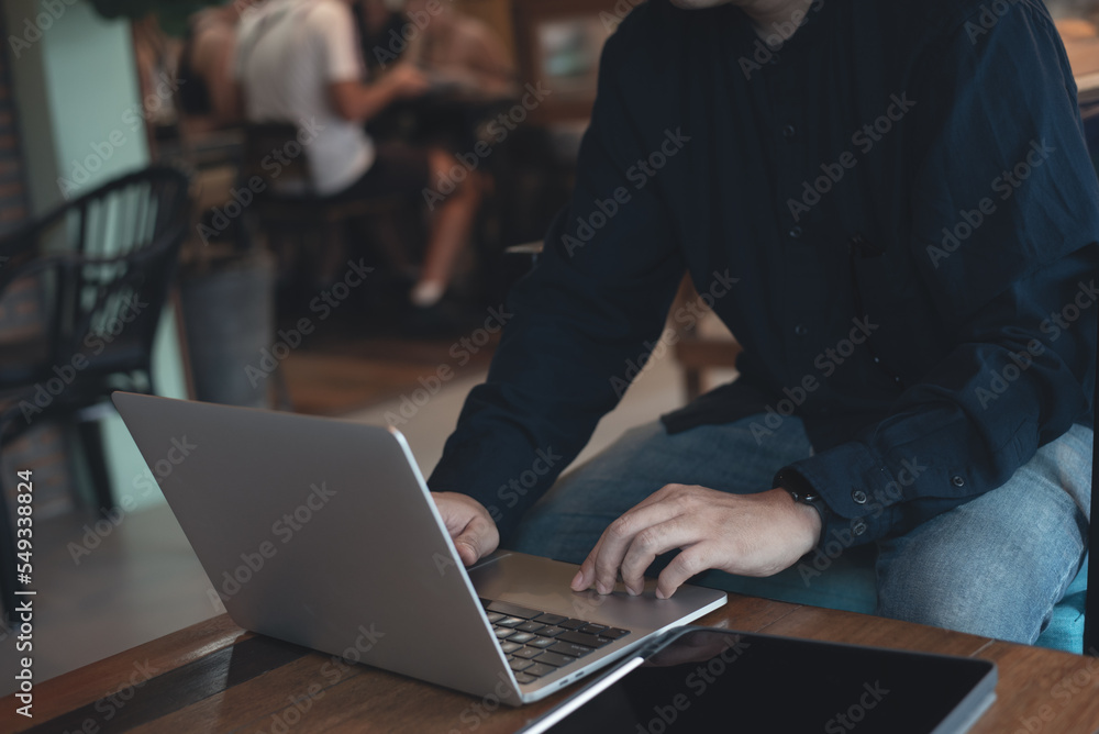 Poster man working on laptop computer and using digital tablet surfing the internet on wooden table at coff