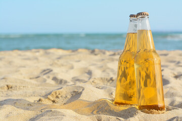 Fototapeta na wymiar Bottles of cold beer on sandy beach near sea, space for text