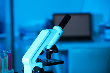 Modern microscope with glass slide in laboratory, toned in blue. Space for text
