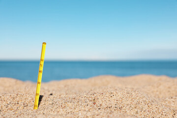 Yellow weather thermometer in sand near sea, space for text