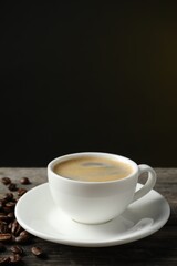 Cup of hot aromatic coffee and roasted beans on wooden table against dark background