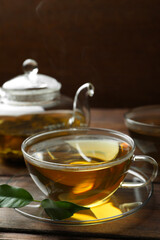 Fresh green tea in glass cups, leaves and teapot on wooden table