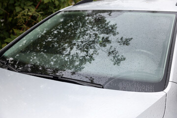 Wipers cleaning raindrops from car windshield outdoors