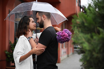 Young couple with umbrella enjoying time together under rain on city street, space for text