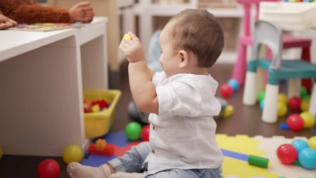 Adorable toddler playing with toys sitting on floor at kindergarten