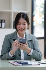 Pretty Asian business woman in black suit working at her office desk, with document file and paperwork. texting mobile smartphone or chat message