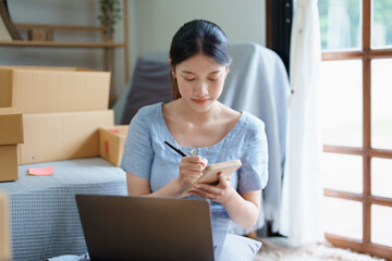 Starting small business entrepreneur of independent young Asian woman online seller is using computer and taking orders to pack products for delivery to customers. SME delivery concept