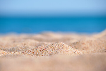 Fototapeta na wymiar Close up of clean yellow sand surface covering seaside beach with blue sea water on background. Travel and vacations concept