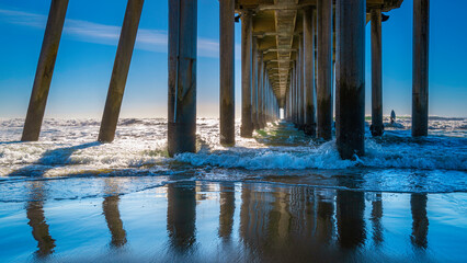 Sea waves and water reflections of boardwalk underside, abstract geometry of Huntington Beach Pier...