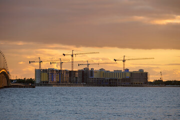 Obraz premium Tower cranes and frame structure of high residential apartment buildings at construction site on sea bay shore. Real estate development at waterfront