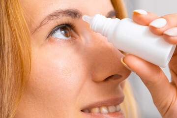 Close up a young blonde hair woman applying eye drops. Drops to lubricate dry eyes.